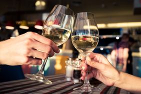 Two people toasting with glasses of white wine indoors focus on hands and glasses
