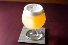 A glass of beer with foam served on a coaster on a wooden table