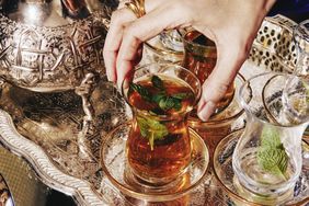 Tray with glasses of mint tea ornate teapot and a hand holding a glass adorned with fresh mint leaves