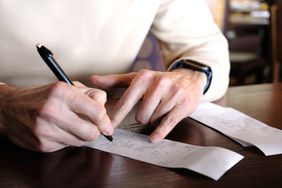 A person reviewing and writing on a receipt using a pen on a wooden table