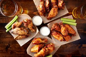 Overhead view of four different flavored chicken wings with ranch dressing, beer, and celery sticks.