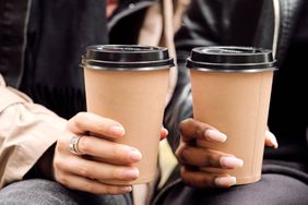 Two hands holding coffee cups with lids closeup