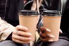 Two hands holding coffee cups with lids closeup