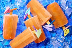 Five icy popsicles with small paper planes attached resting on ice