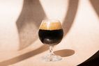 A glass of dark beer, on a beige background with shadows.