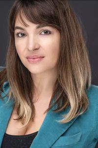 Prairie Rose headshot, wearing teal blazer on grey background