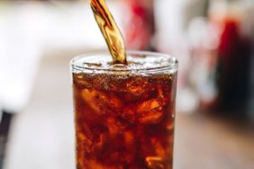 A glass filled with iced soda being poured on a blurred table background