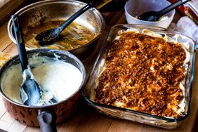 A prepared lasagna dish next to bowls with components such as sauce and cheese mixture on a countertop