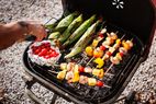 Skewered kebabs corn and foilwrapped vegetables on a barbecue grill with someone inspecting food with tongs