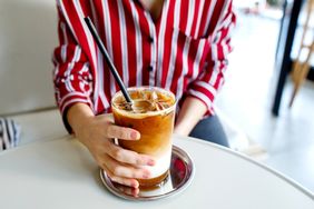 A person holding a glass of iced coffee with layers of milk and espresso sitting at a table