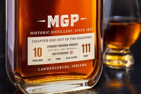 A bottle of MGP straight bourbon whiskey aged 10 years with a glass of whiskey in the background