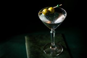 A martini glass with olives on a toothpick placed on a surface