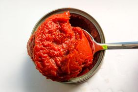 A spoon scooping tomato paste from a can showing its texture and consistency