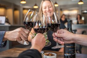 Group clinking wine glasses indoors bottle of wine on table