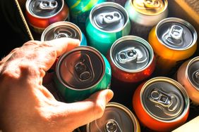 A hand selecting a soda can from a collection of cans in a box