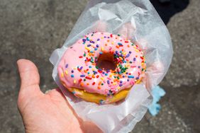 A person holding a donut with pink frosting and sprinkles