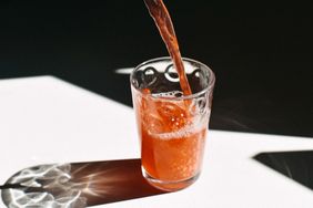 Pouring a beverage into a glass on a table with light reflections cast around the glass