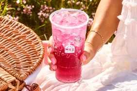 A hand holding a Taco Bell Baja Blast drink in a clear plastic cup with a picnic setup nearby