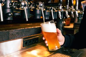 A hand holding a beer glass being filled from a tap in a bar setting