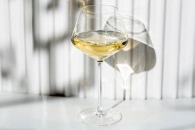 A glass of white wine on a surface with vertical shadows in the background