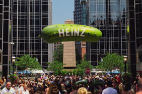 A crowded outdoor festival with a large pickleshaped balloon with Heinz written on it