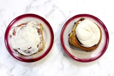 Two cinnamon buns on plates with white icing on top