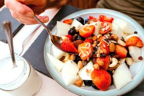 Bowl of fruit and nut salad with a spoon accompanied by a jar of yogurt