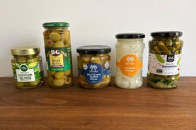 Five jars of assorted olives and pickled garnishes displayed on a wooden surface