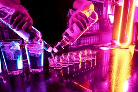 Person pouring drinks in a bar setting with bright colorful lighting