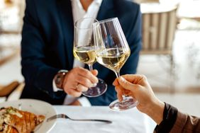Two hands holding wine glasses for a toast at a dining table with a meal