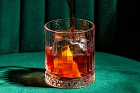 A glass with an ice cube being filled with a beverage