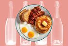 A plate with two eggs, toast, bacon and buttered pancakes over a background of sparkling wine bottles. 