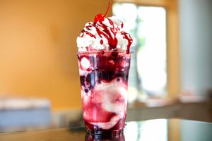 Ice cream sundae topped with whipped cream fruit sauce and a cherry