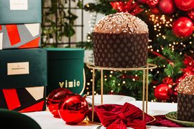 A panettone on a stand surrounded by festive decorations and gift boxes