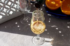 A glass being filled with a lightcolored beverage slices of orange in the background