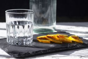 A glass of clear liquid next to orange slices on a slate platter