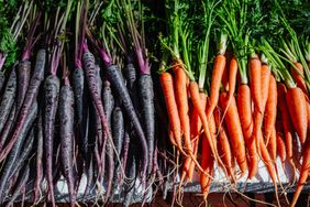 Two rows of carrots one purple and one orange with greens attached