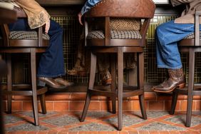 Three individuals wearing cowboy boots seated at a bar with stools and a patterned tiled floor