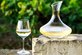 A decanter and a wine glass filled with white wine on an outdoor surface